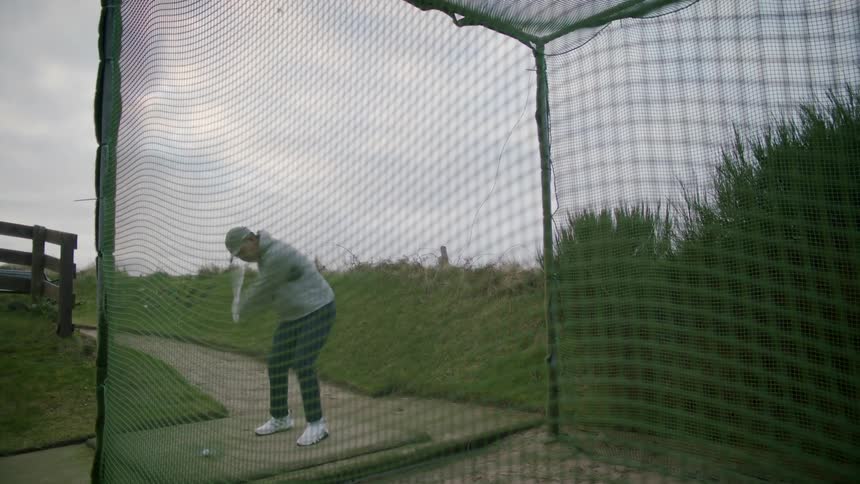 Man swings golf club in to practice net outdoors