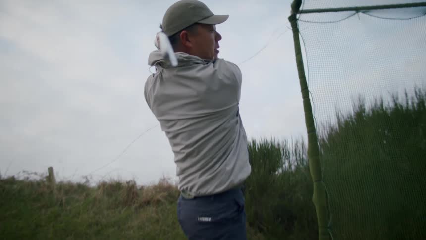 A man drives a golf ball into a net as he practices his swing on a cloudy day