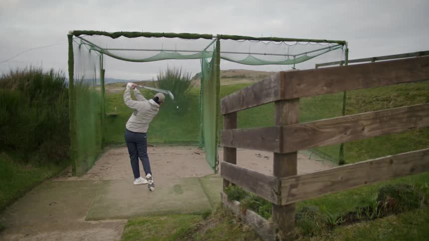 A man swinging at a golf ball into a golf net in the course