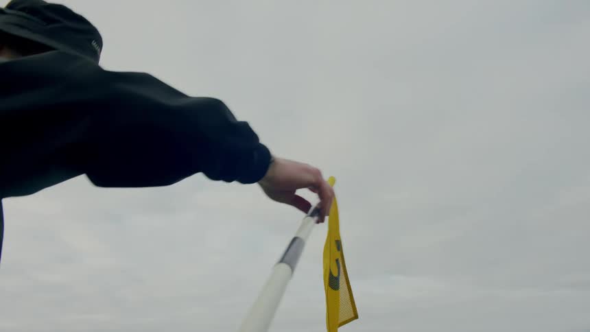 Man wearing a hat outdoors on a golf field lifts up a yellow flag from the ground while two other man walk nearby
