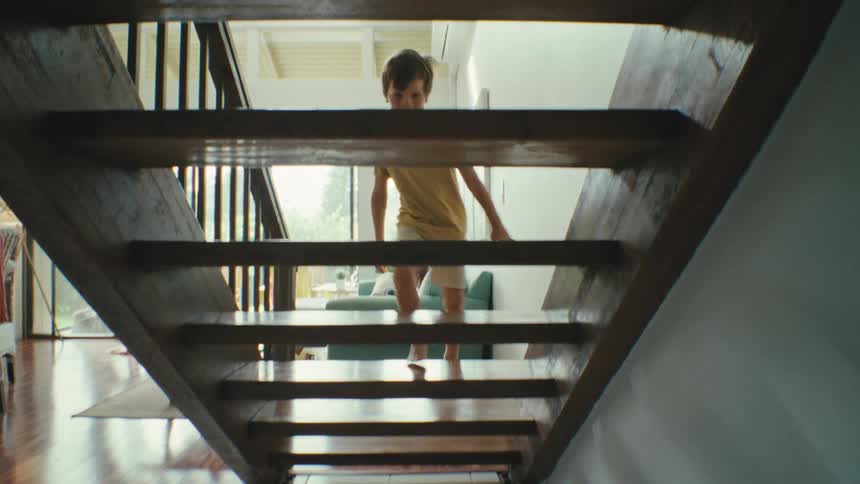 Boy in a yellow tshirt and shorts running up a wooden staircase at home