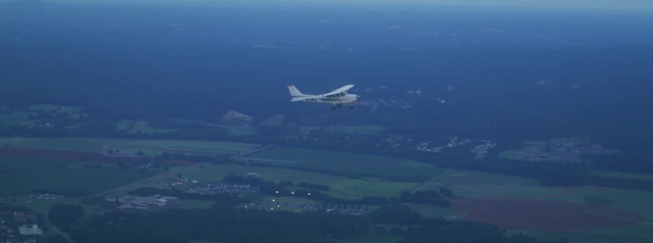 A small plane flying over the land with a cloudy sky