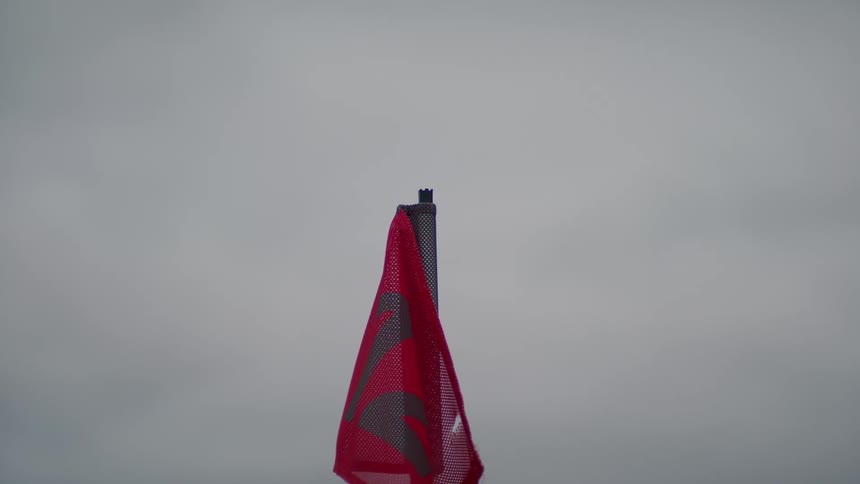 A red and black flag hangs from a pole and sways in the wind on a cloudy day