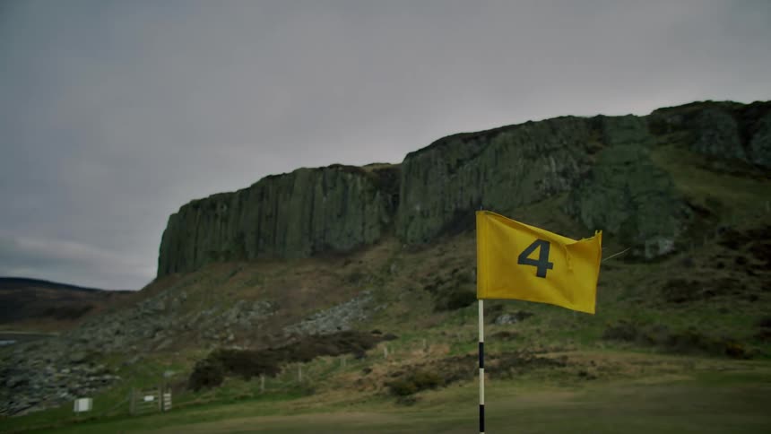 A yellow flag with the digit four on the front on a golf fairway