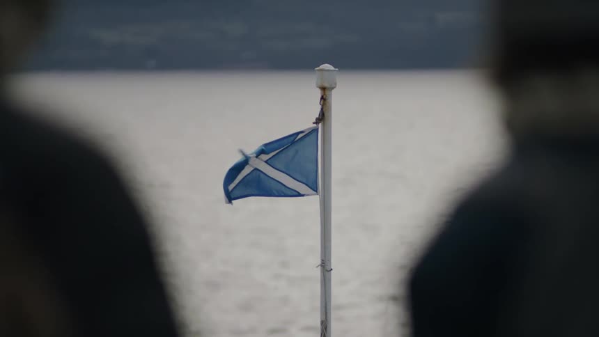 A flag waving on a pole out over some water