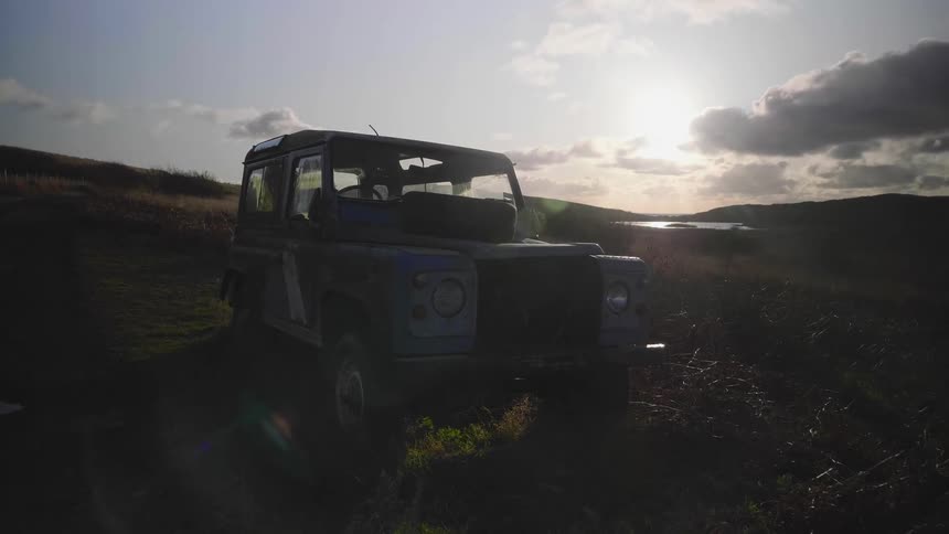A jeep parked on a grassy field with the sun shining behind it