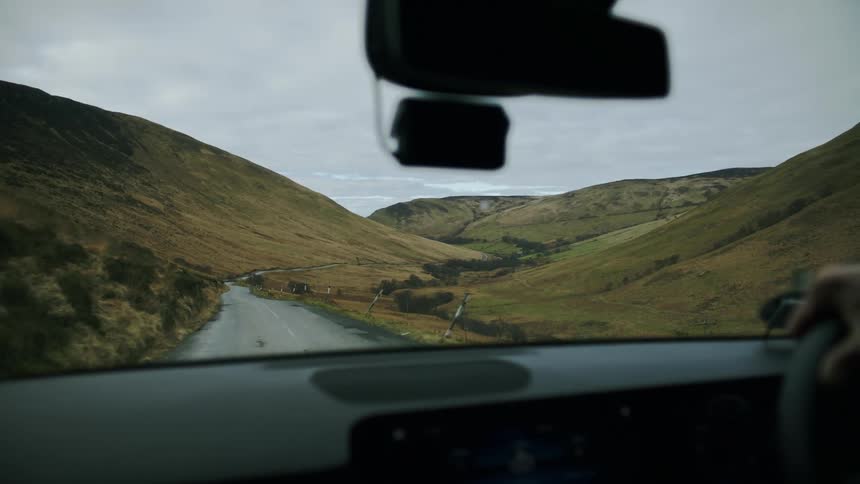 A person driving a car on a deserted road between mountains