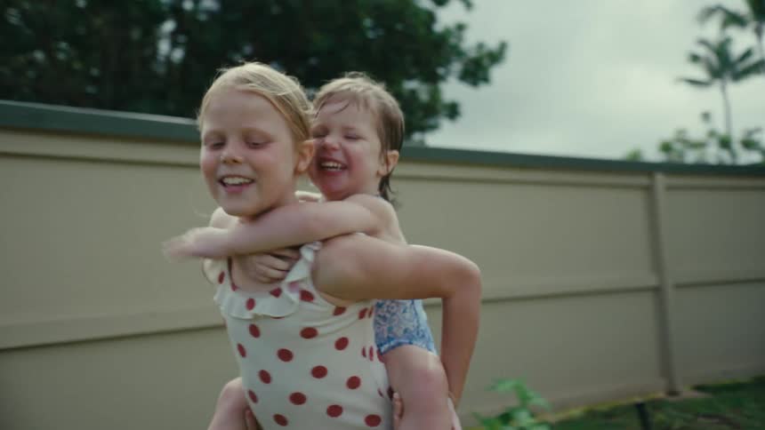 Girl wearing swimsuit carrying her little sister on her back in the backyard
