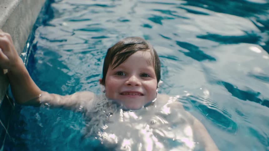 Toddler boy swimming on a pool outdoors smiling on a sunny day