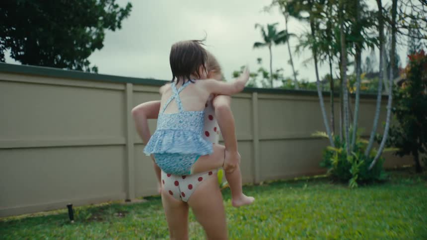 A female child backs her sister while playing on the backyard lawn at daytime