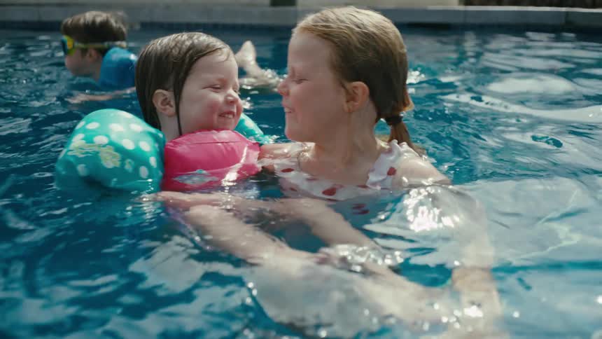 An older child teaching a toddler how to swim in a pool