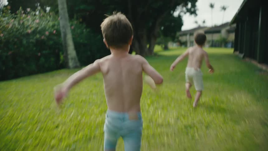 Two shirtless boys chasing each other in the backyard