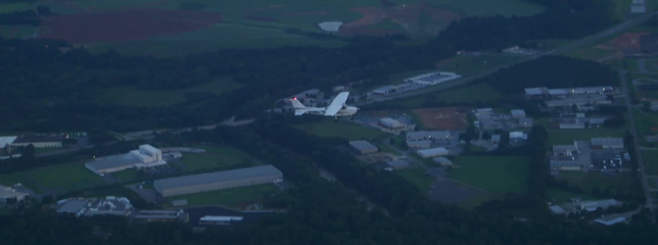Aerial view of white airplane flying through an urban area surrounded by vegetation