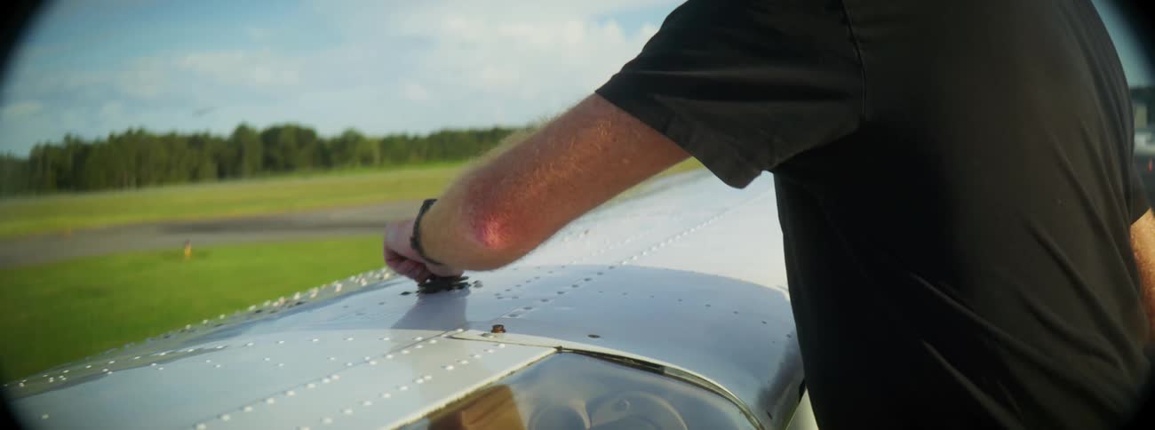 A man uses a dropper to add fluid to an airplane wing on a summer day