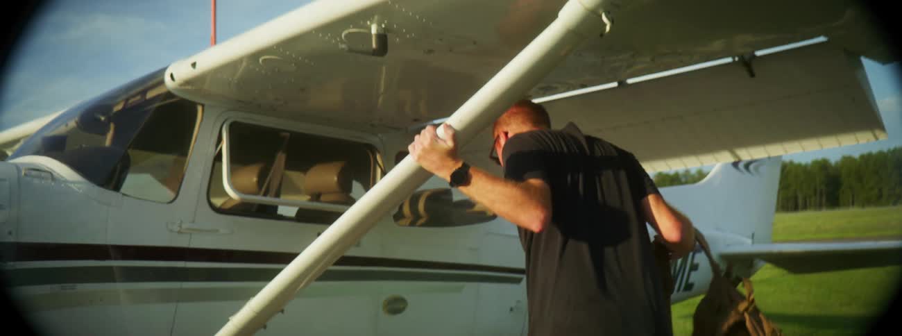 Man carrying a large backpack boards an small airplane on an airfield