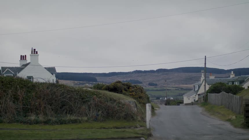 A road leading to a white house and hills under a cloudy sky