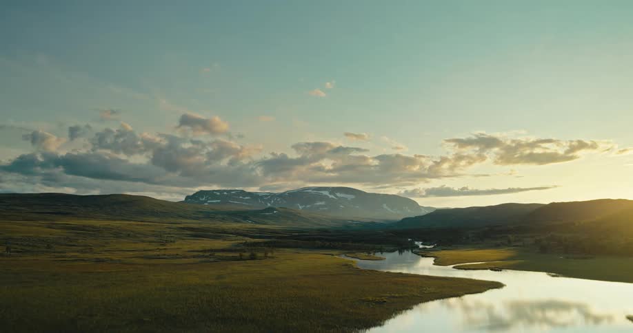 Aerial view of a grass field with river streams around and mountains on the background during dusk or dawn