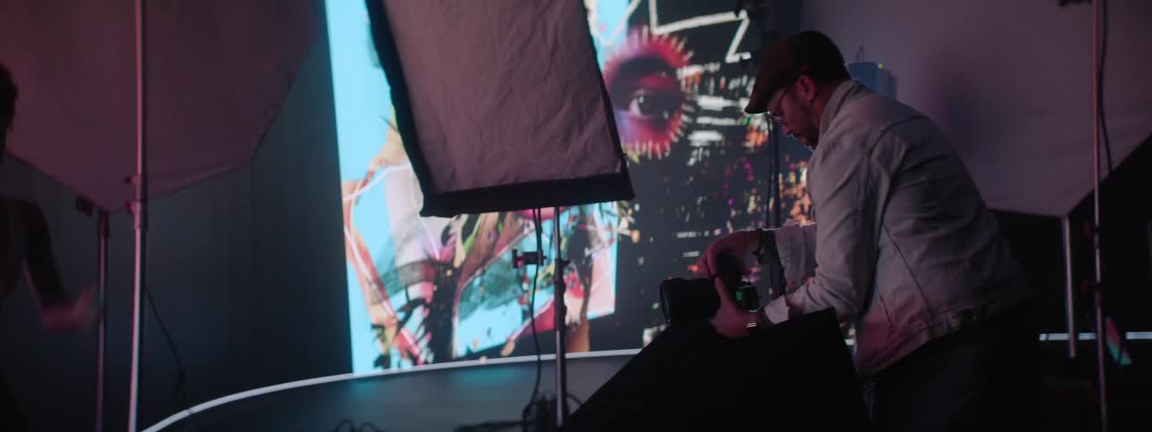 A person is working on a photography set adjusting a camera with a large image projected in the background