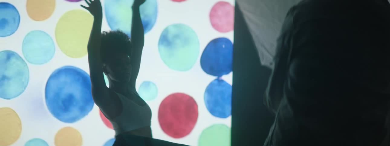 A dancer poses in front of a flashing projection screen while being photographed