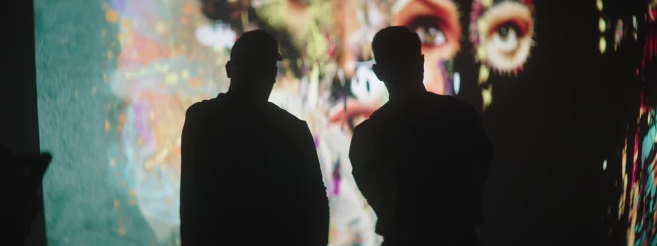 Silhouette of two men talking in front of a large projector