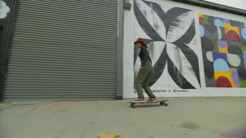 A woman skateboards on an la sidewalk past colorful urban art murals
