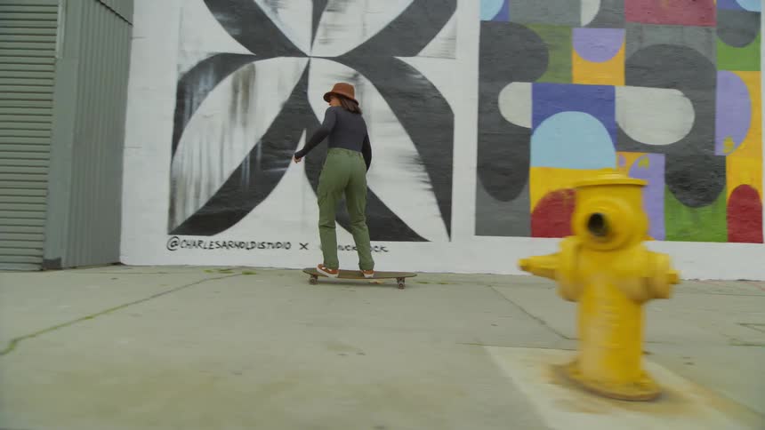 A woman skateboards in front of a wall with various abstract and geometric murals