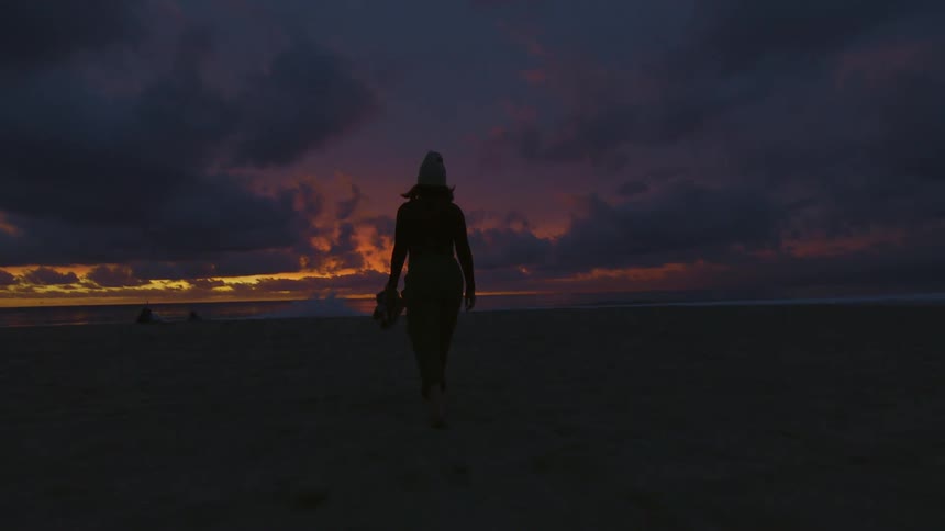 Silhouette of a woman walking towards the beach at sunset