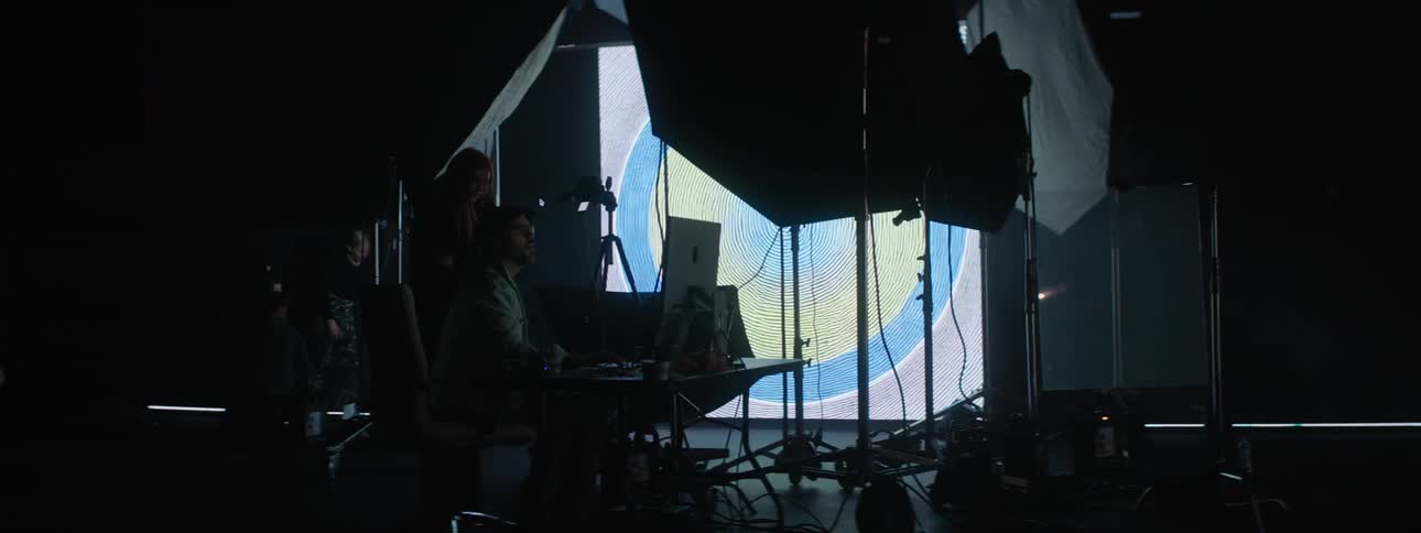 People working on laptops in a photography set with a large projector in the background