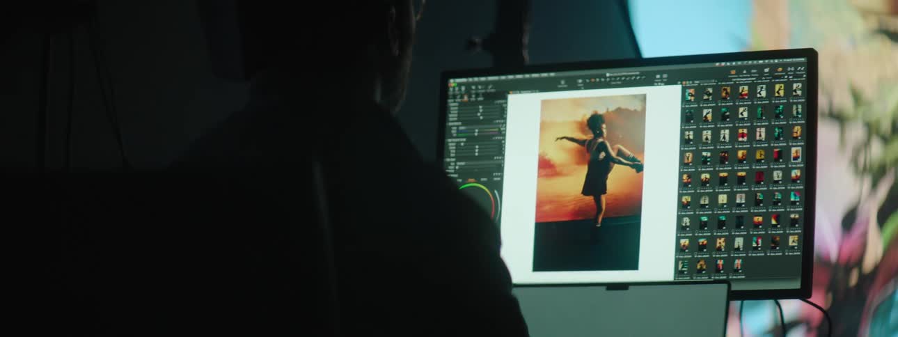 A black man is staring at pictures of a dancer on a computer monitor