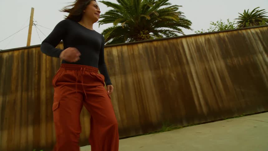 Woman rides a skateboard on the sidewalk next to a wooden fence