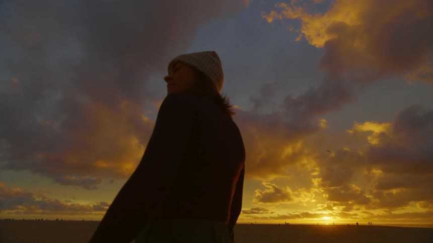 Woman standing on the beach at sunset spins around