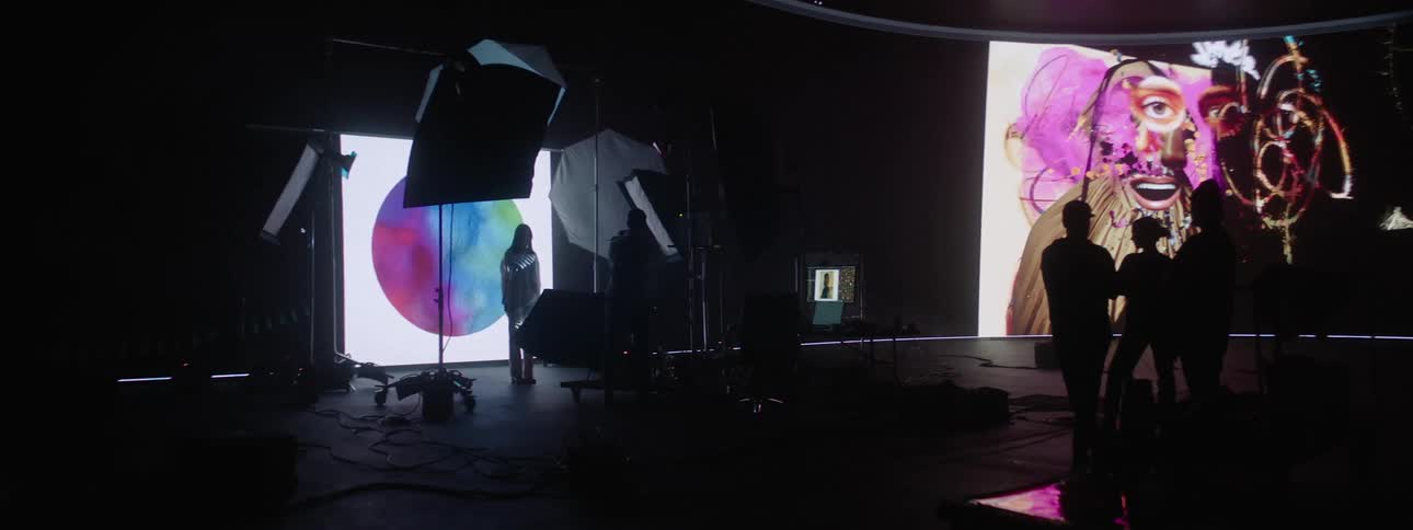 A female modeling in front of large screen playing videos while others are in the room