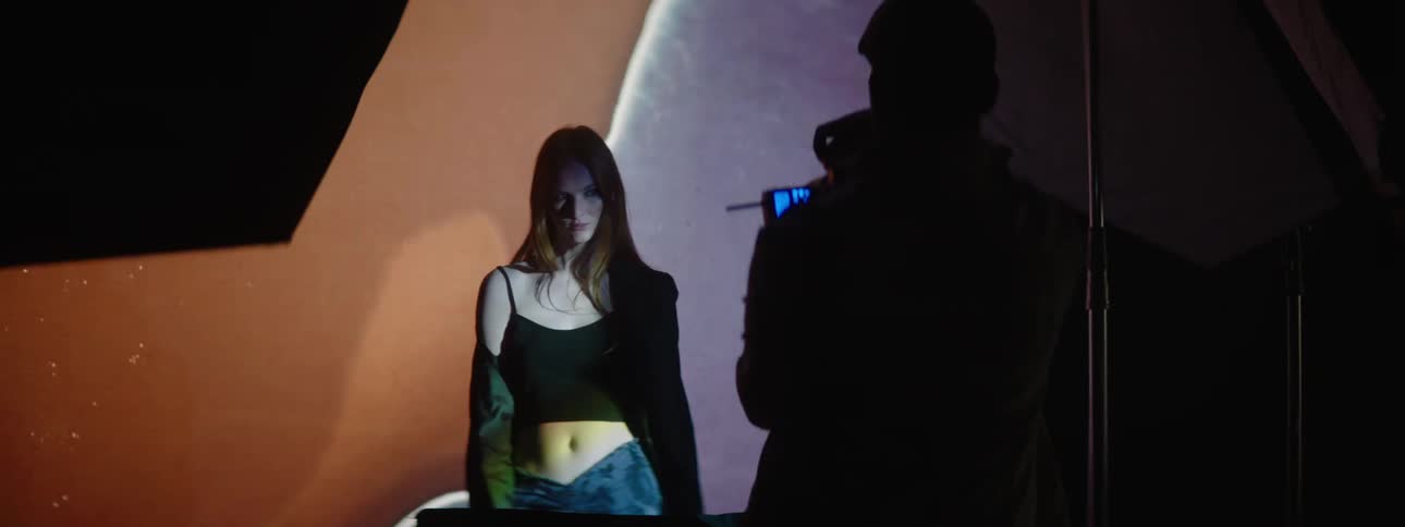 A female posing for a photographer in front of a large screen playing a video
