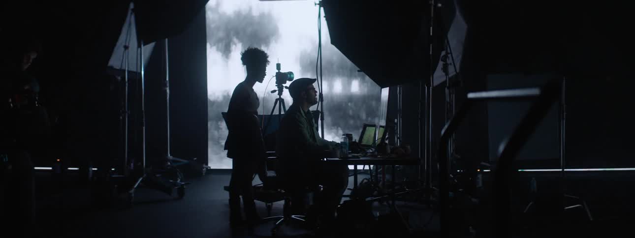 Two people in front of laptop screens viewing images projected on the wall in a dark room
