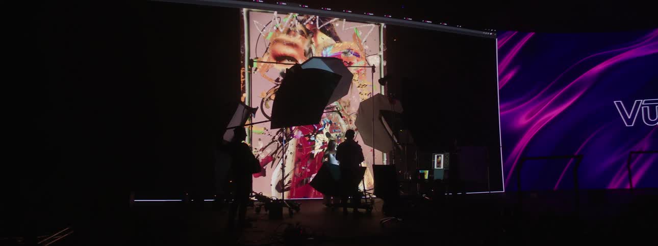 Three people in a studio taking photos of a model in a dark room with a video projected in the background