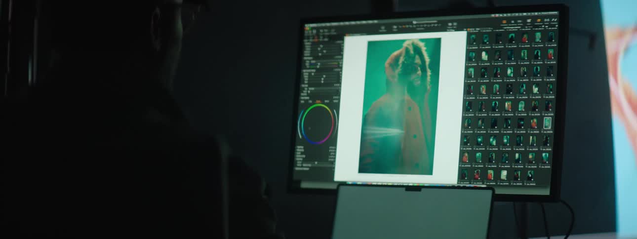 Man with glasses editing pictures on a computer in a dimly lit room