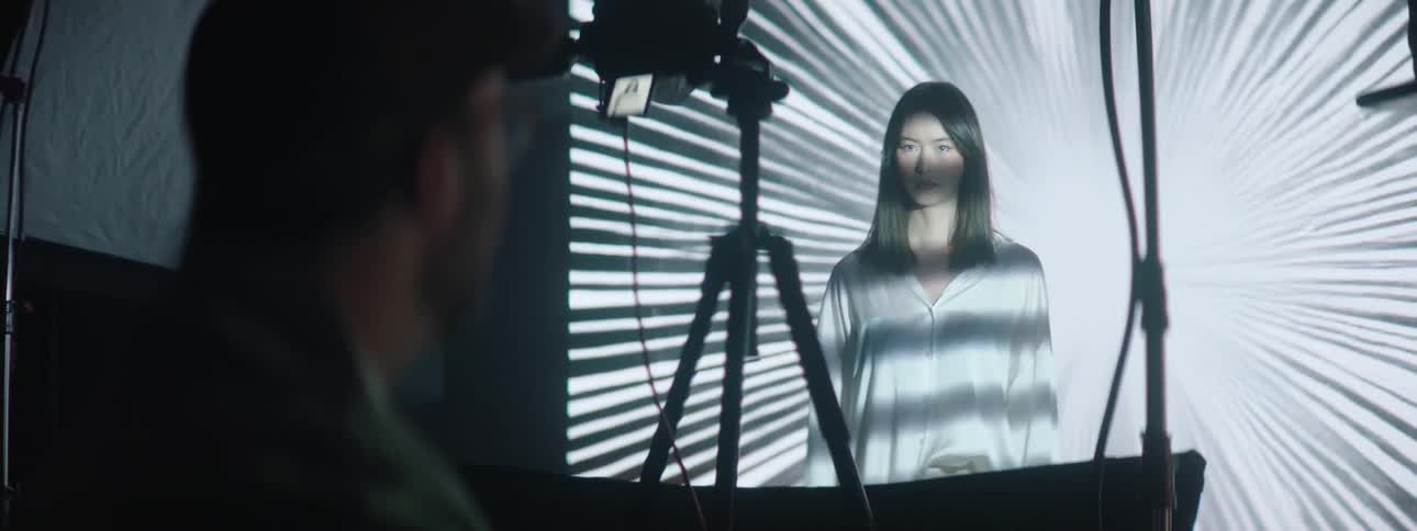 Photographer takes pictures of a model in front of a large projector in the background