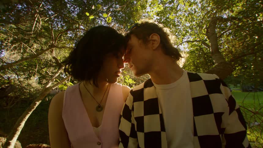 Man and woman lean their heads together while sitting on tree near field on a sunny day