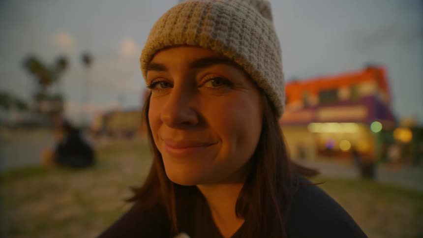 Close up of the face of a young woman wearing a beanie at sunset