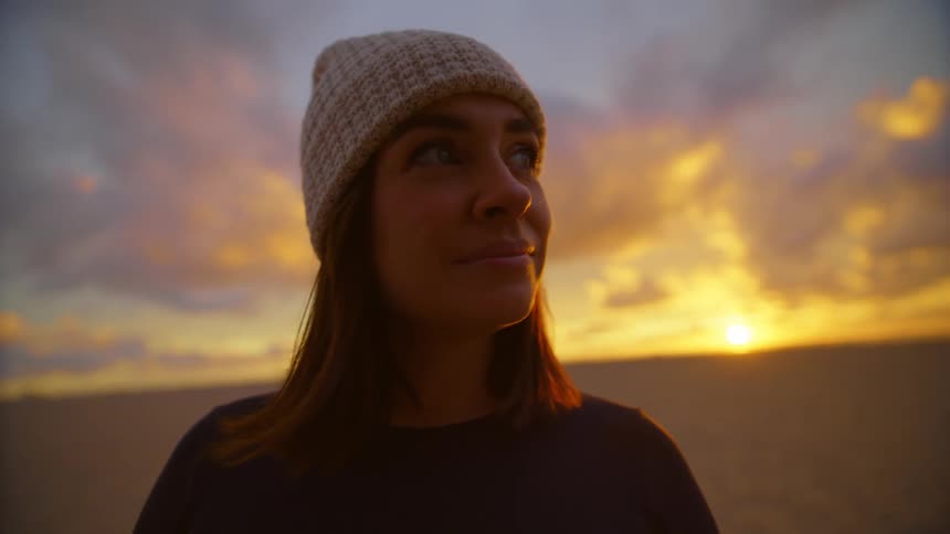 Close up of the face of a woman standing next to the ocean at sunset