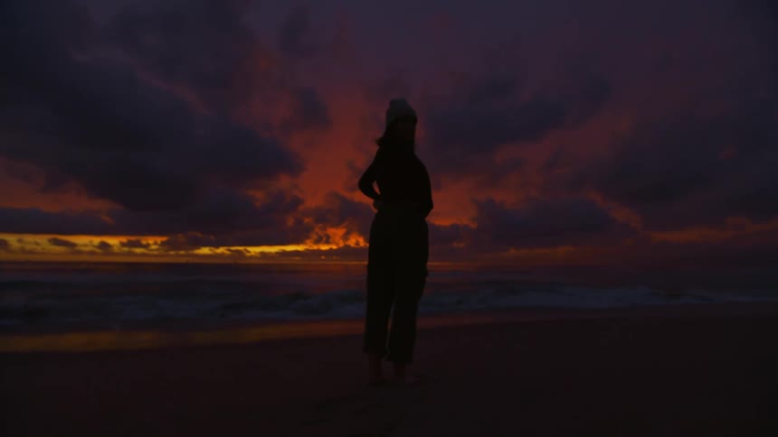 Silhouette of a woman standing on a beach looking at the red sky at sunset