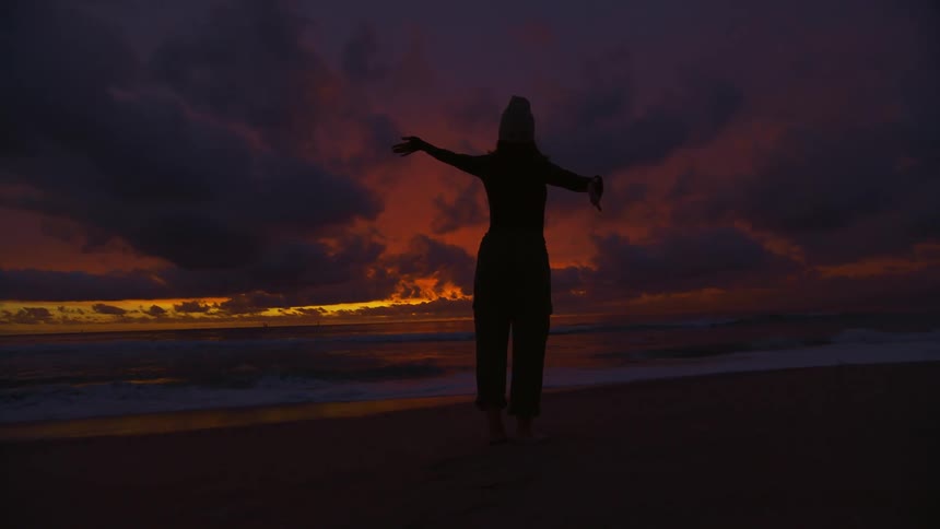 Silhouette of a woman standing on the beach at sunset