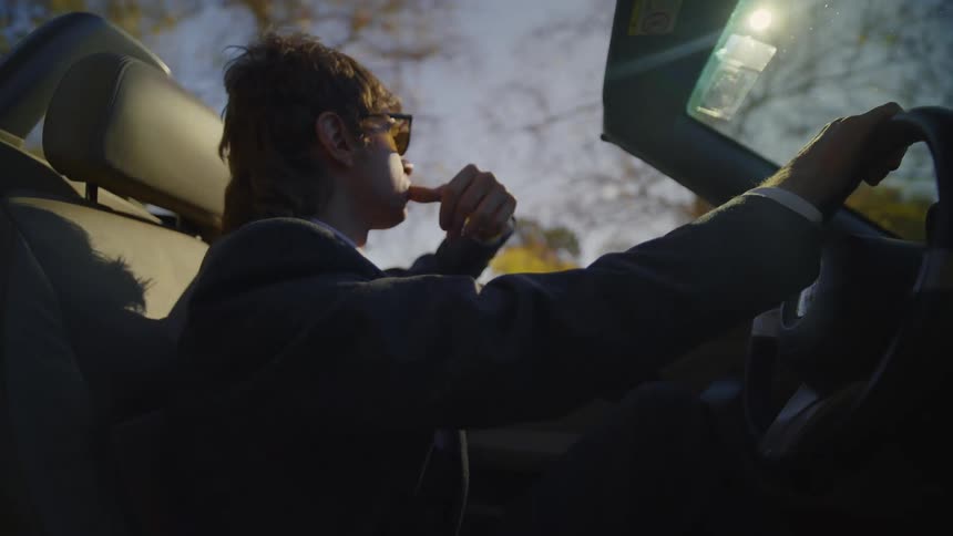 Young man wearing sunglasses drives a convertible car