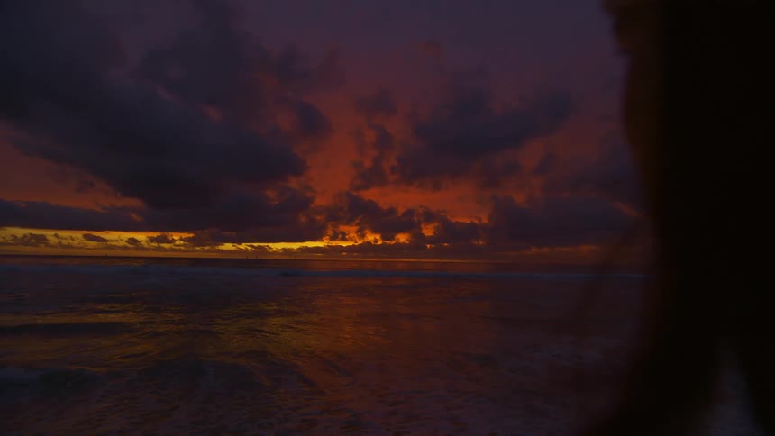 Woman stands on beach looking out to the horizon during sunset as the waves roll onto shore