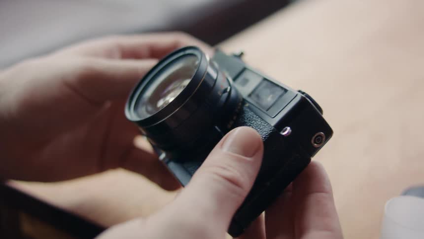 A person holds a small camera in their hands and inspects all sides of it