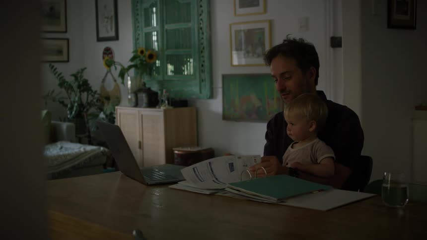 A father working on his laptop with his son in his arms