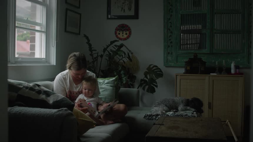 Mother reading a story book with her baby in the living room