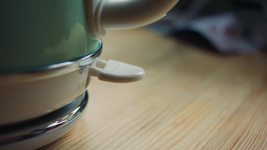 A hand reaches out to press down the switch turning on an electric kettle