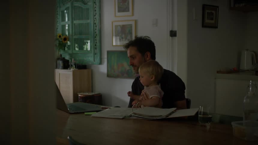 A clip of a father babysitting a toddler while working on his laptop
