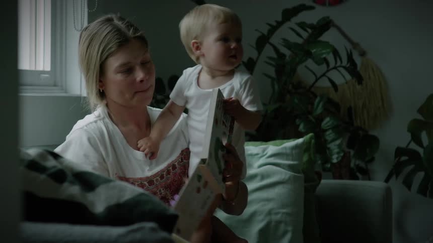 Mother sitting on the sofa with her baby on her lap reading a book